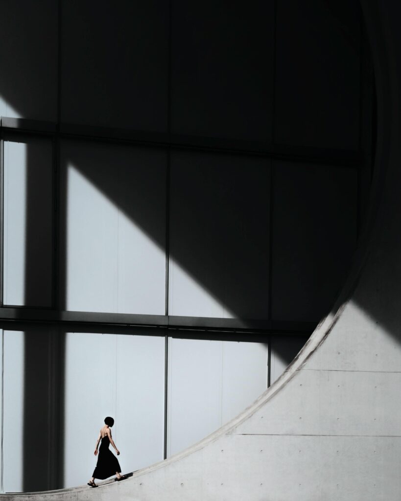 A woman walking near the iconic geometry of Berlin's modern architecture, creating a dramatic silhouette in sunlight and shadow.